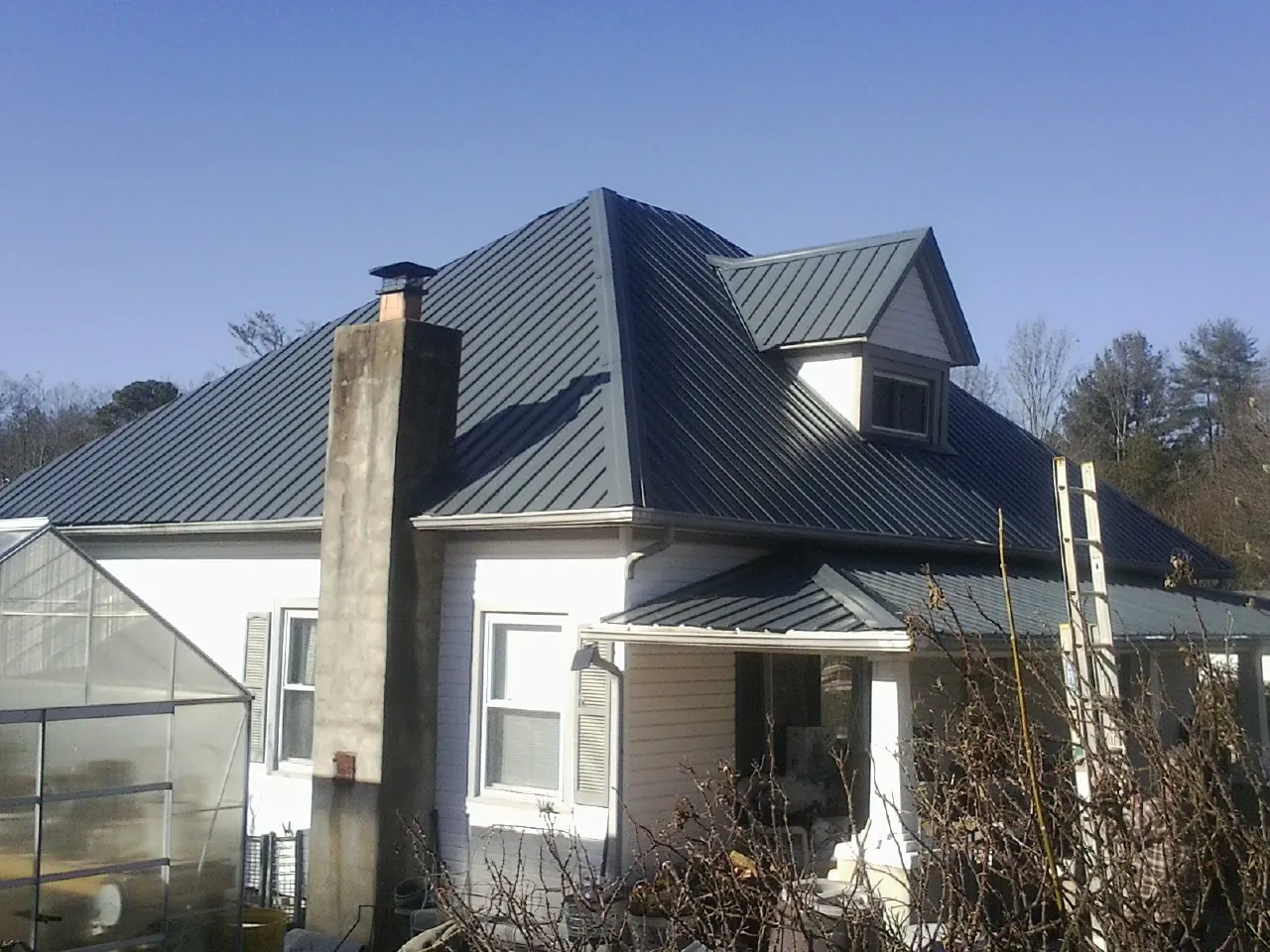 Dark blue standing seam metal roof on a white farmhouse with dormer — Slate & Tile Roof Repair by Roofing Brothers in Mc Ewen