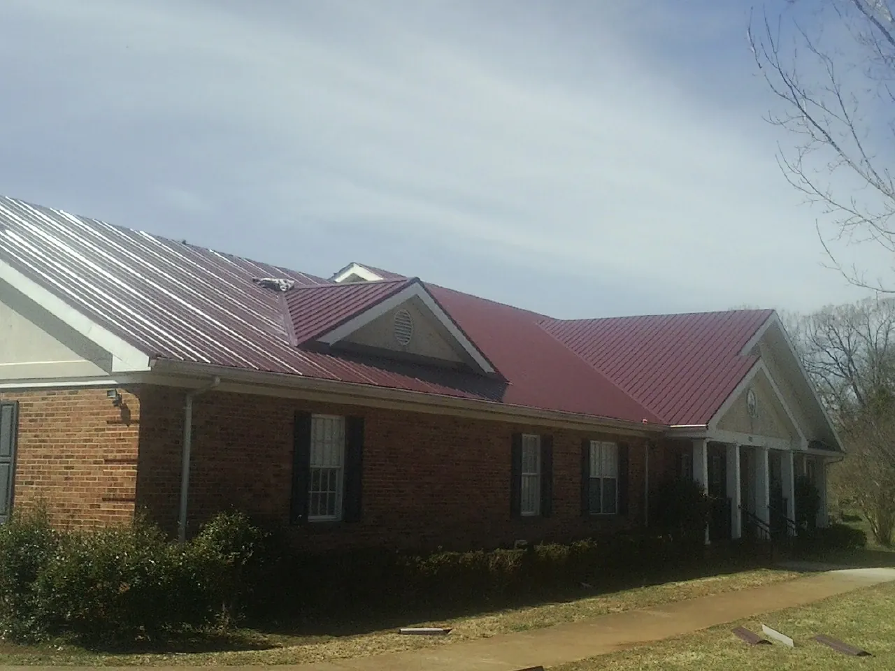 Red metal roof with gabled entries on a long brick building, from a Hail Damage Roof Repair job in Mc Ewen