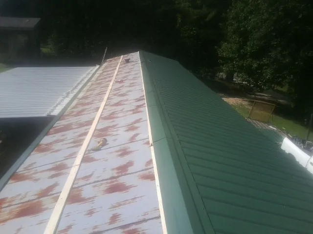 Old rusted panels beside newly installed green metal roofing — Wind Damage Roof Repair by Roofing Brothers in Mc Ewen