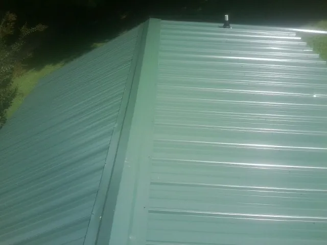 New green metal panels meeting at the ridge of a roof — Flat Roof Repair work by our crew in Mc Ewen