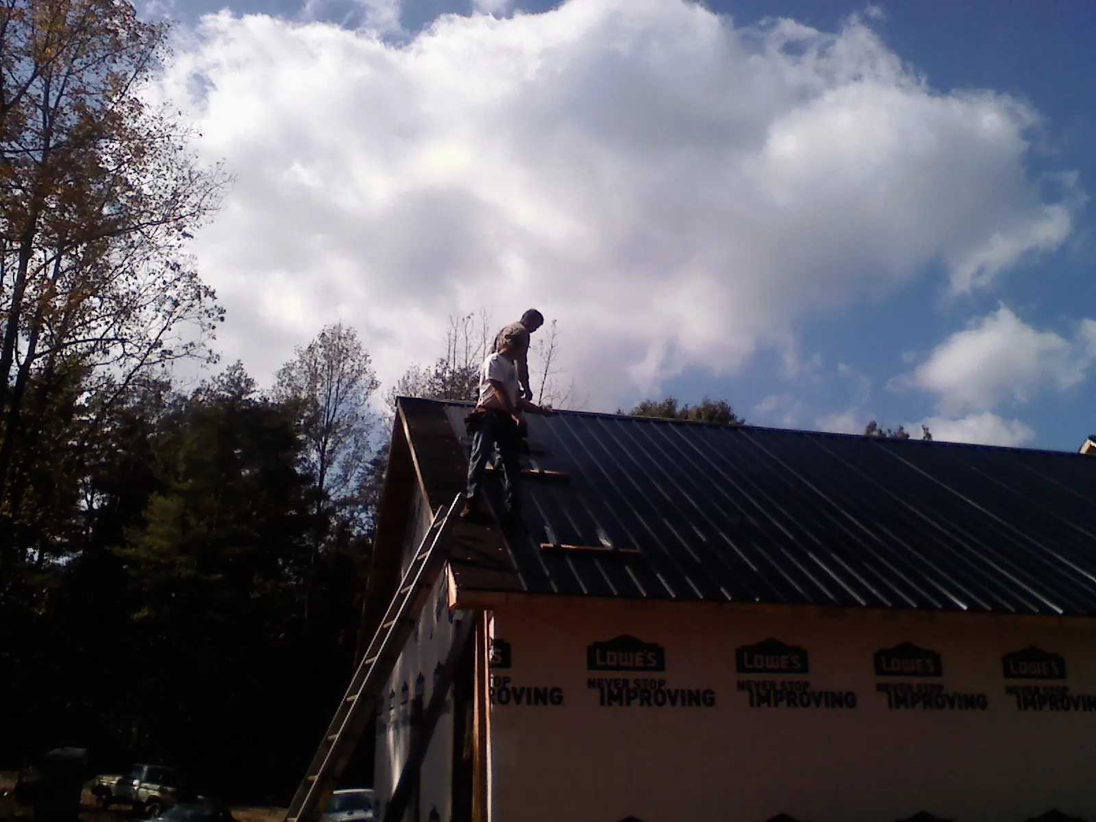 Roofer fastening dark metal panels high against a cloudy sky, from a Roof Inspection job in Mc Ewen