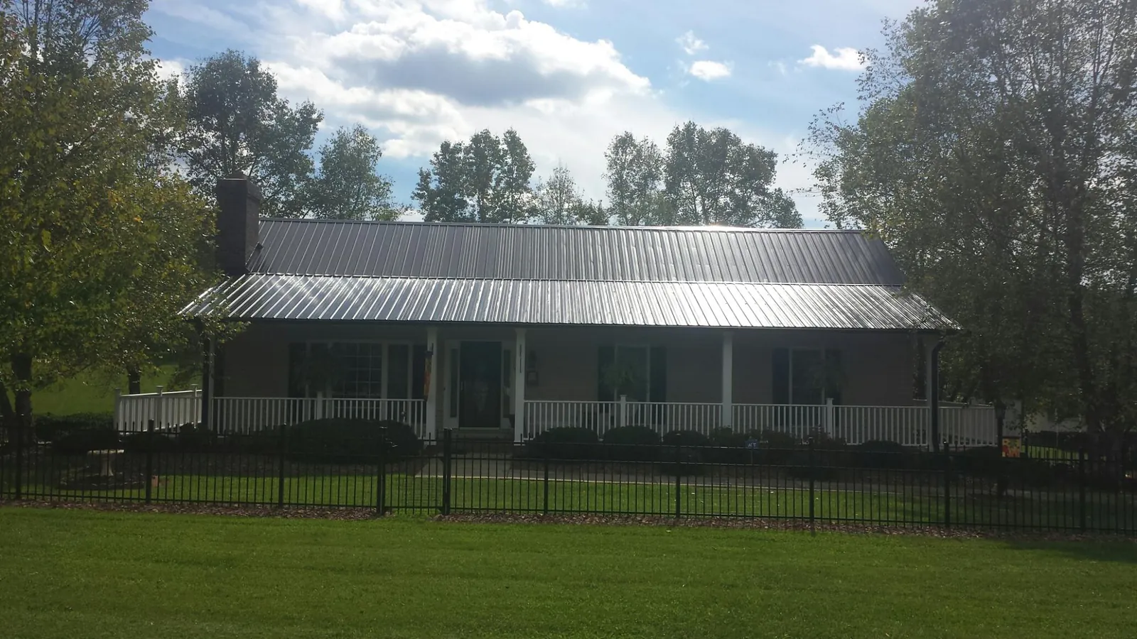 Gray metal roof on a brick ranch with a full width front porch — Gutter Guard Installation work by our crew in Mc Ewen