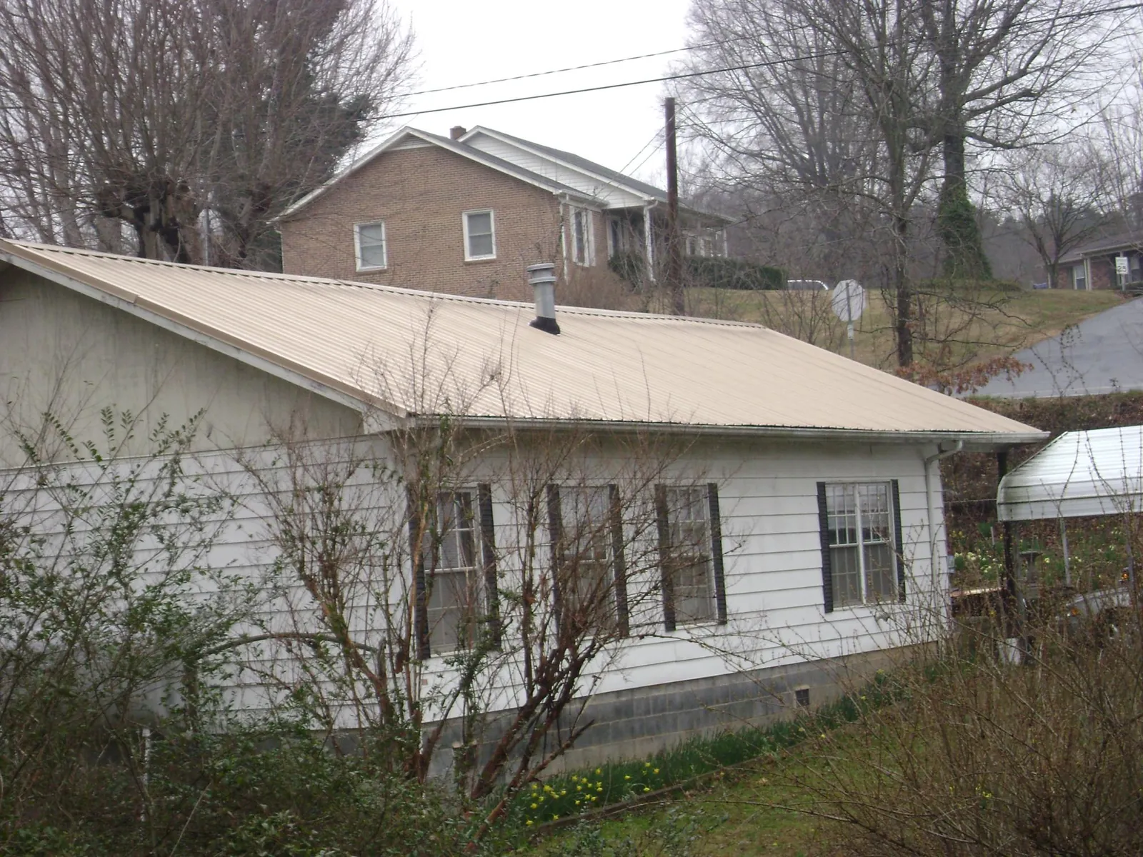 Tan metal roof on a white sided house set into a hillside — Commercial Roofing by Roofing Brothers in Mc Ewen